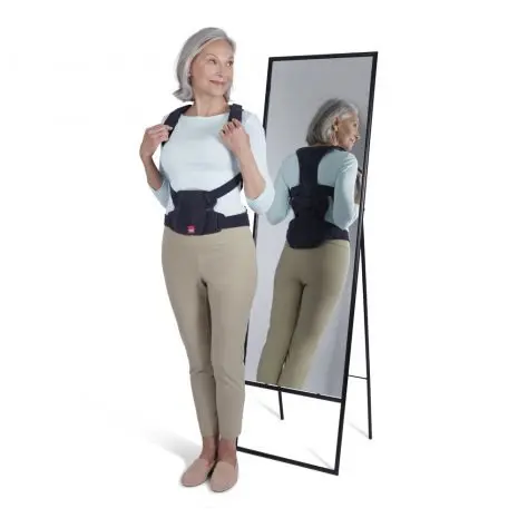 Senior woman adjusting posture brace in mirror.